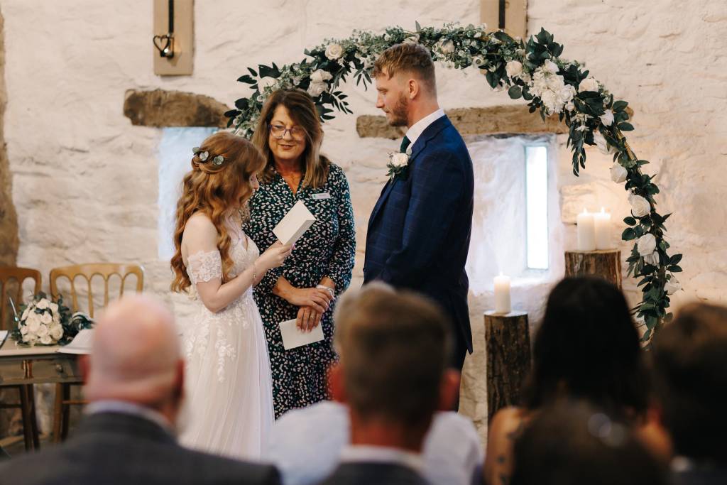 Jane leading a wedding ceremony under a floral arch