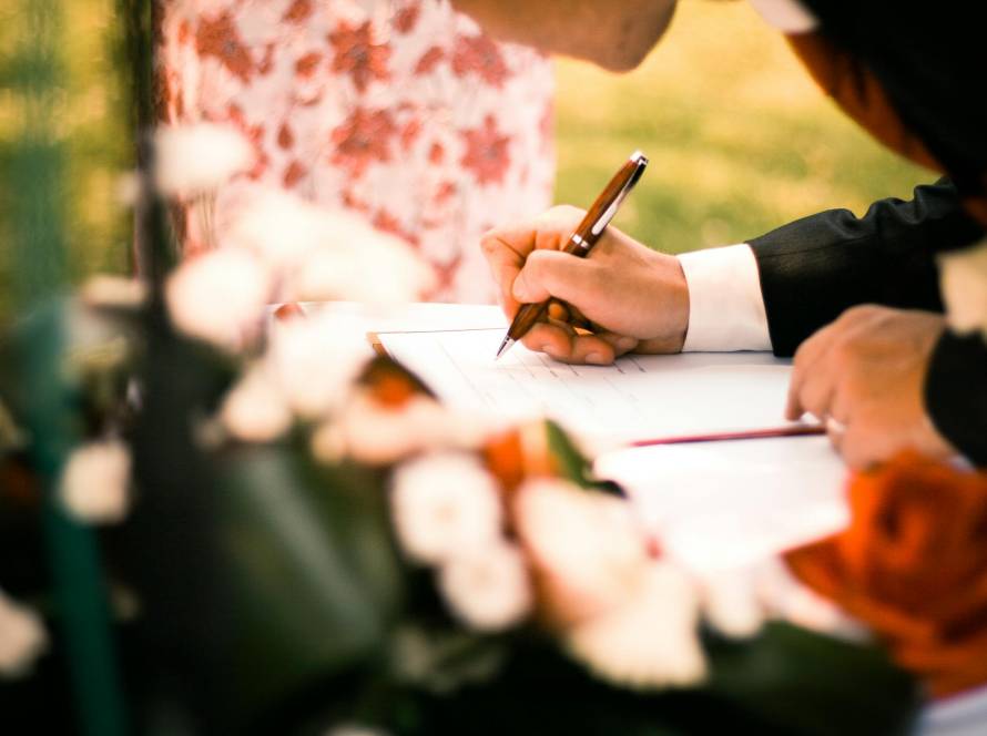 A close-up of hands signing a marriage contract during an outdoor wedding ceremony