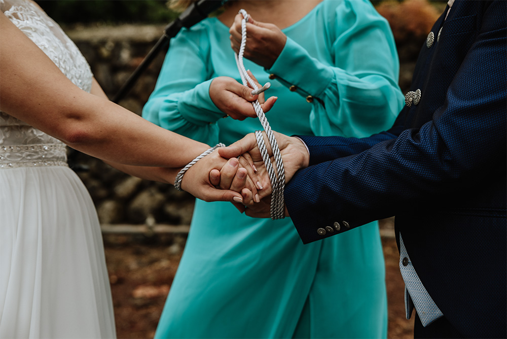 Couple’s hands wrapped in ribbons during a handfasting ceremony led by Jane