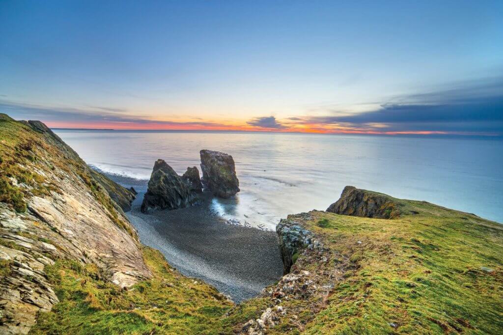 Sea stacks and a pebble cove below grassy cliffs on the North Wales coast at sunset