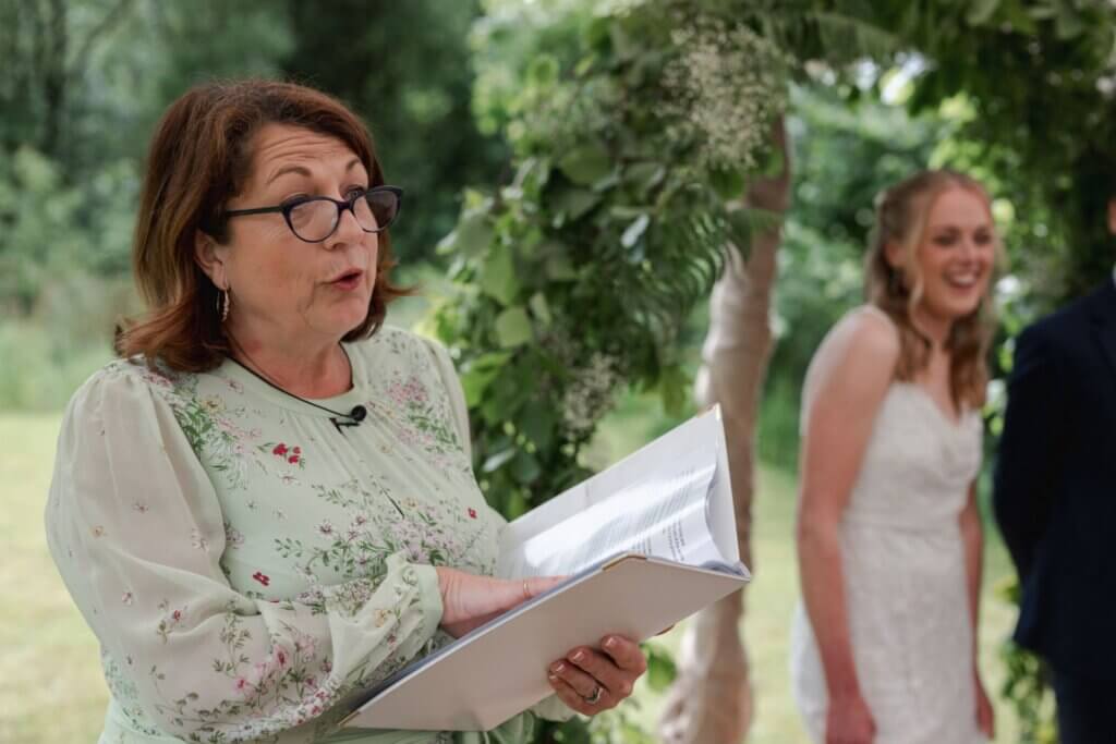 Celebrant Jane Jones reading the couple’s story from her folder while the bride smiles in the background