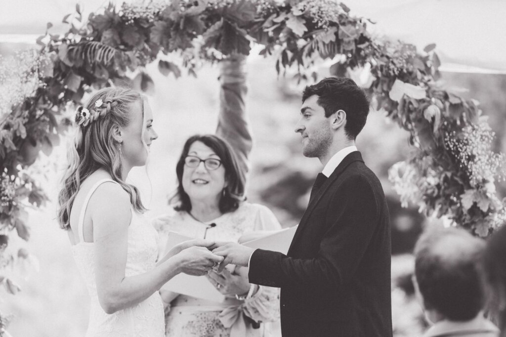 Black and white photo of a bride and groom holding hands and smiling at each other as celebrant Jane Jones looks on